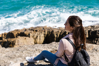 Side view of woman sitting on rock at beach