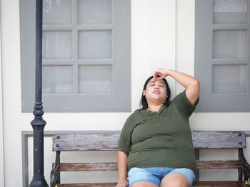 Tired overweight woman with eyes closed sitting on bench against window