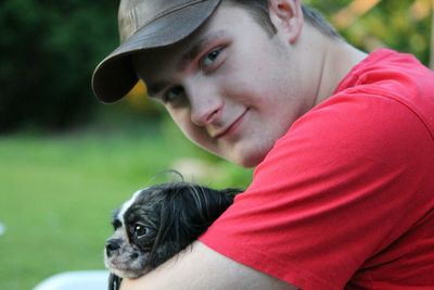 Portrait of young man holding dog at field