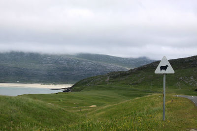 Road sign on landscape against cloudy sky