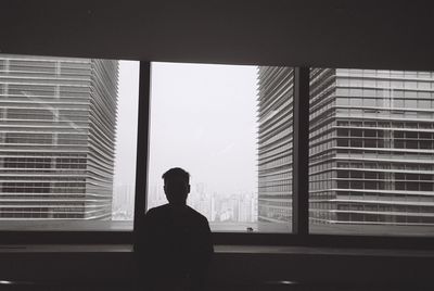 Rear view of silhouette man looking through window