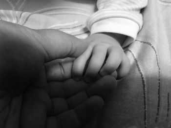 Cropped hand of parent and baby boy on bed