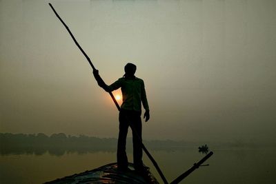 Silhouette man fishing in water against sky