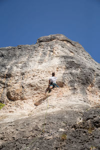 Low angle view of man rock climbing against sky