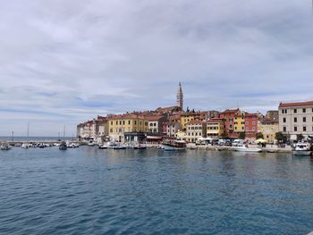 Sailboats in sea by buildings in town against sky