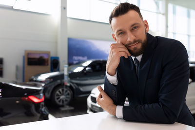 Handsome salesman leaning on table in car showroom