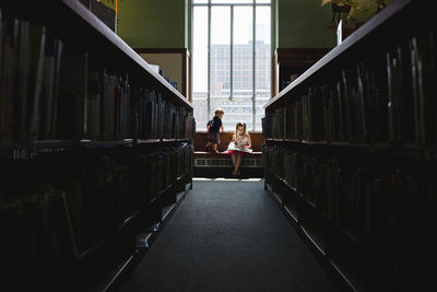 Boy looking at sister reading book by window in library