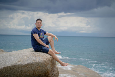 Full length of man on rock in sea against sky