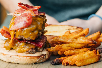 Close-up of double cheeseburger with bacon next to french fries on wooden board