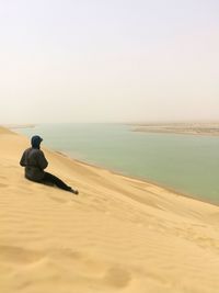 Man sitting on sand while looking at sea