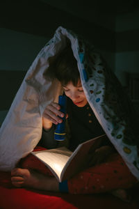 Boy reading book with flashlight in darkroom