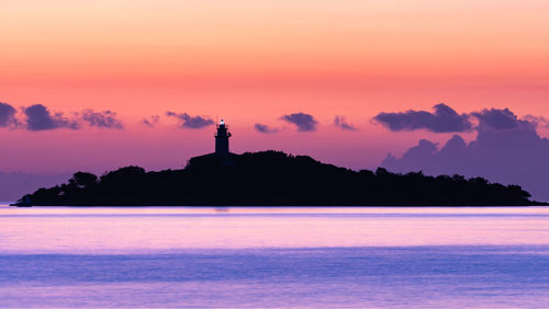 Silhouette lighthouse by sea against sky during sunset