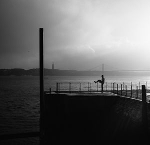 Man on pier by tagus river against cloudy sky