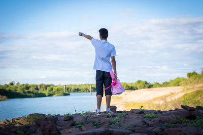 Rear view of man standing on rock against sky