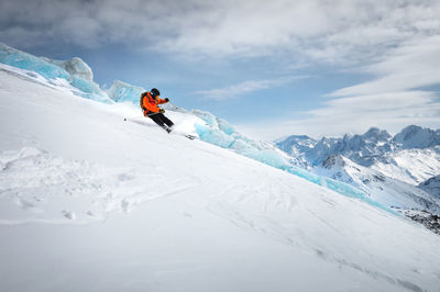 Off-piste skier on a glacier going down a beautiful alpine landscape. blue cloudy sky in the