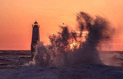 Lighthouse by sea against sky during sunset