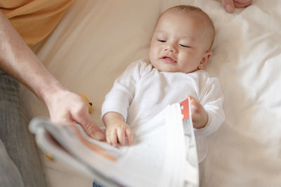 Father showing newspaper to baby on bed at home