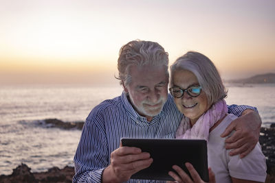 Man using mobile phone at beach against sky during sunset