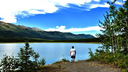 Rear view of man standing on lake against sky
