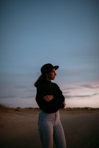 Side view of young woman standing against sky during sunset