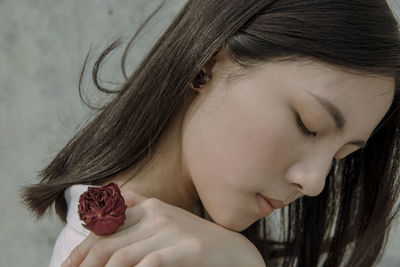 Close-up of young woman wearing rose shape ring against wall