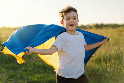 Ukrainian child boy in white t shirt with yellow and blue flag of ukraine in field.