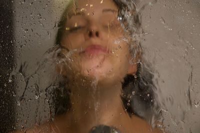 Close-up of woman bathing in bathroom seen through window