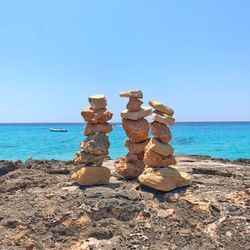 Stack of pebbles on beach against clear blue sky