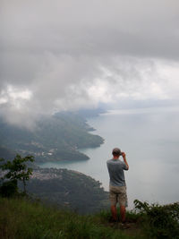 Rear view of man standing on mountain against sky