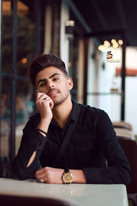 Portrait of young man looking away while sitting on table