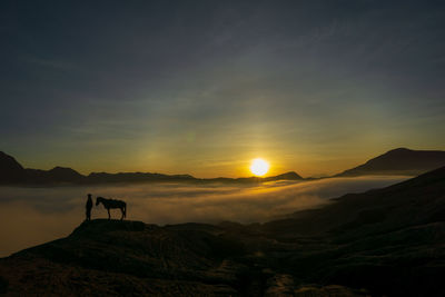 Silhouette person standing on mountain against sky during sunset