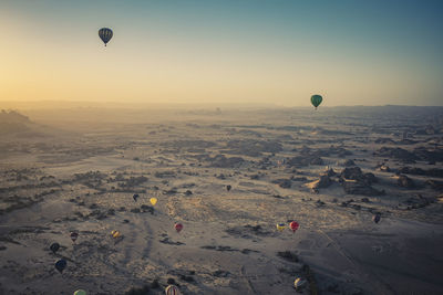 Hot air balloons flying over landscape against sky during sunset