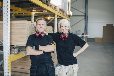 Portrait of smiling male and female workers standing by rack in industry