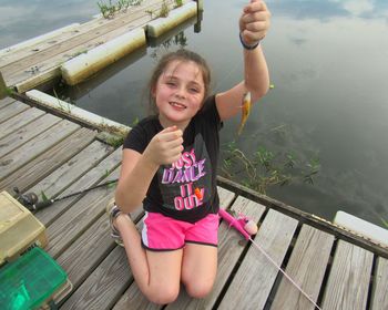 High angle portrait of girl holding fish while sitting on jetty by lake