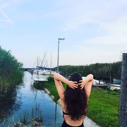 Rear view of woman standing by lake against sky