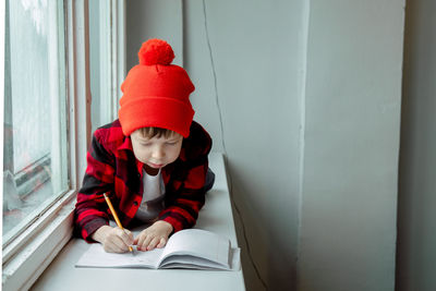 Boy does homework. the boy lies on the windowsill and writes in a notebook. home schooling.