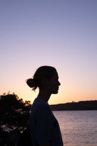 Side view of woman standing against clear sky during sunset