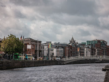 Buildings by river against cloudy sky