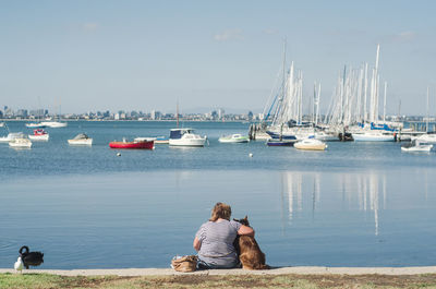 Rear view of women sitting at harbor against sky