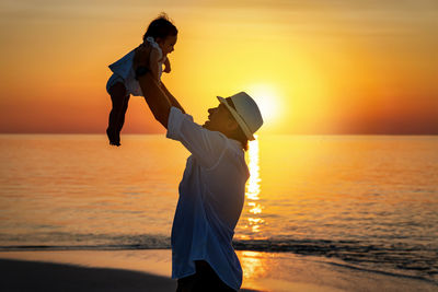 Side view of father playing with daughter while standing at beach during sunset