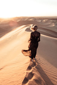 Woman standing on sand dune in desert against sky