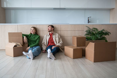 Happy new homeowners renters tired young couple man woman sitting on floor among boxes