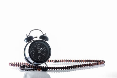 Close-up of alarm clock by prayer beads against white background