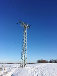 Electricity pylon on snow covered field against blue sky