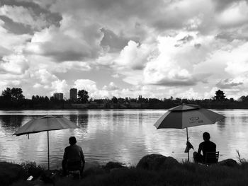 Rear view of men sitting on lake against sky