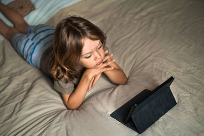 Boy lying on the bed using digital tablet computer playing games or watching cartoons at home.