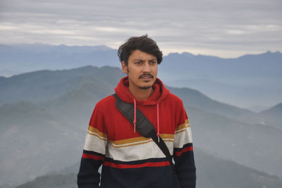 Waist-up of a indian young guy looking sideways while standing against the background of mountains 