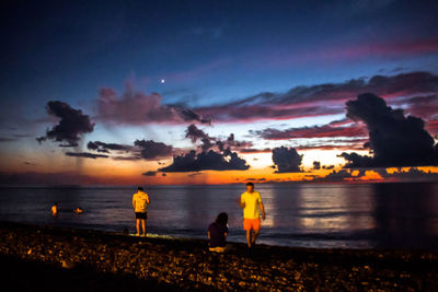 Silhouette people on beach against sky during sunset