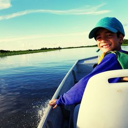 Portrait of smiling boy sitting in boat on lake against sky