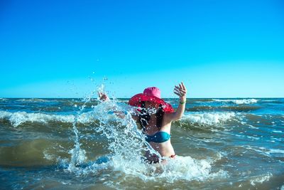 Woman enjoying in water at beach against clear blue sky